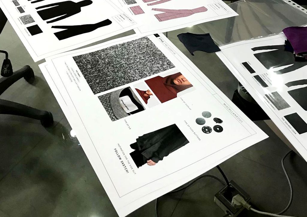 Clothing tech packs for a men's knitwear tops collection on a glass table during a product development session in Pakistan