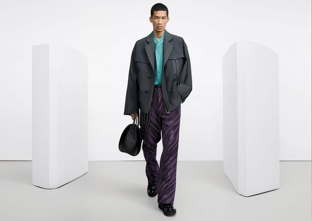 A mixed-race male fashion model walks on a catwalk wearing a grey with purple outfit.